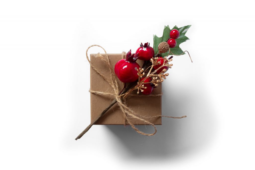 Un pacchetto regalo rivestito di carta marrone e decorato con un ramo di melograno | Photo by Tijana Drndarski on Unsplash