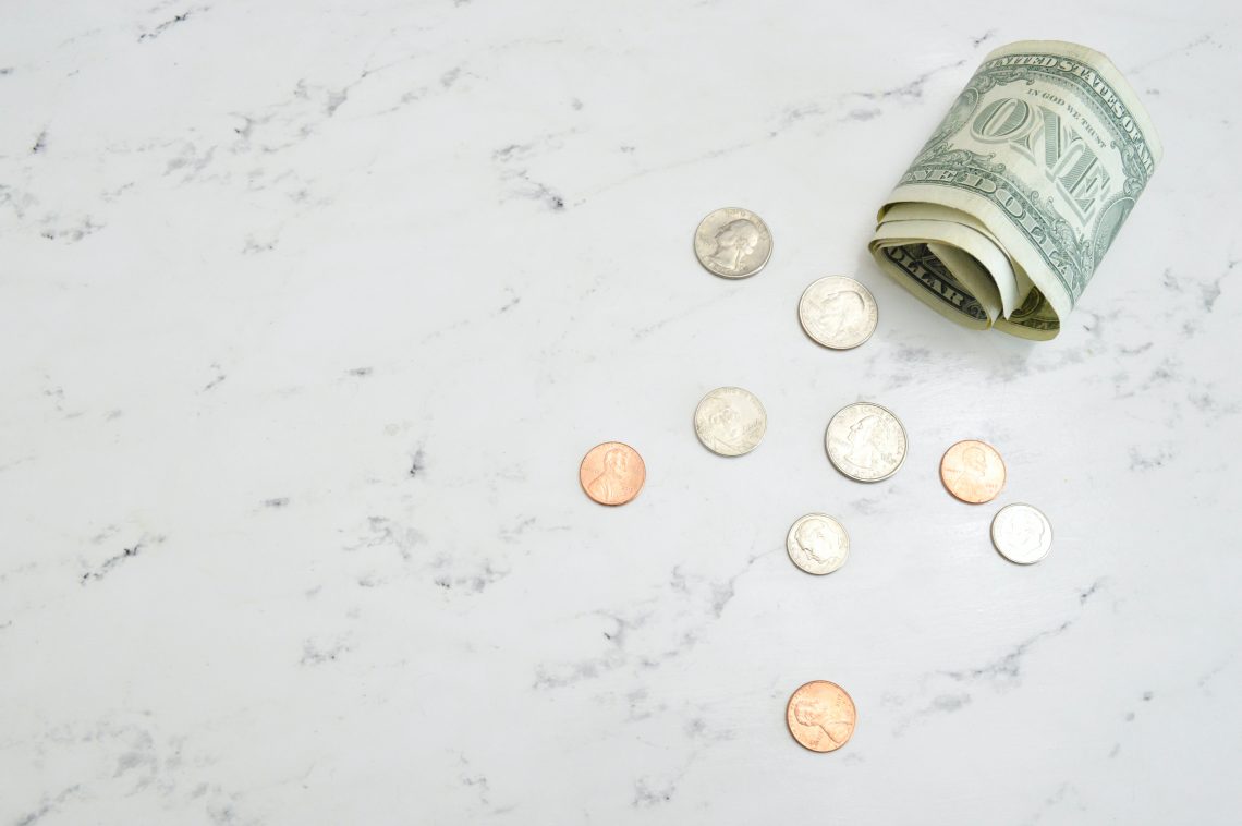 Una banconota da un dollaro e qualche moneta su una superficie di marmo | Photo by Katie Harp on Unsplash